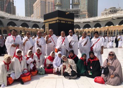 Rombongan jamaah umrah sedang berfoto bersama di area Masjidil Haram, Mekkah, dengan latar belakang Kabah